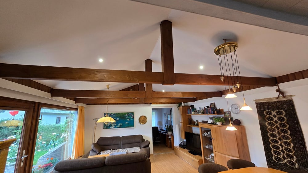 Nachher: weiße Spanndecke mit LED-Spots zwischen den Holzbalken im Wohn- und Essbereich